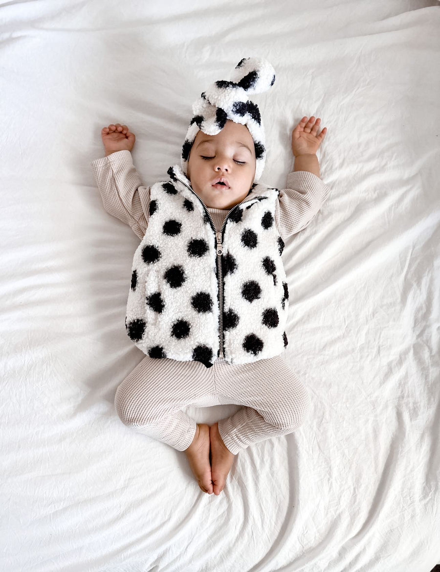 Baby sleeping wearing organic cotton waffle leggings and long sleeved tee in neutral colour-way with a teddy cotton vest in white with black spots and a matching Bobby G headband 