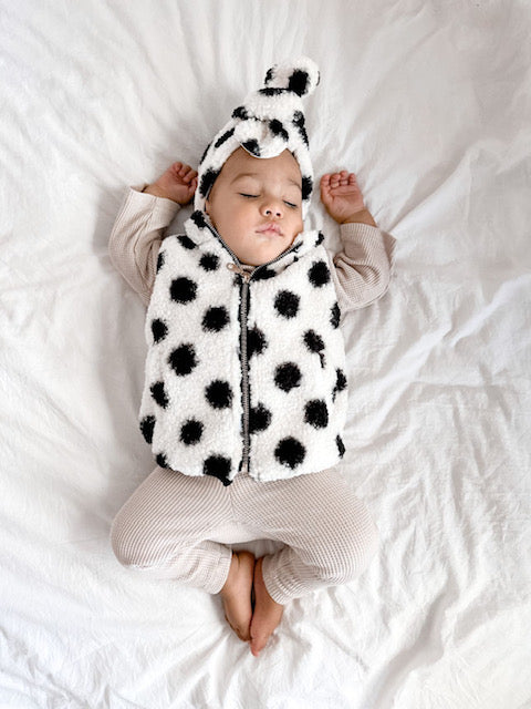 Sleeping baby wearing neutral coloured slim fit leggings and a long sleeved tee paired with teddy cotton vest in white with black spots and a matching headband. 