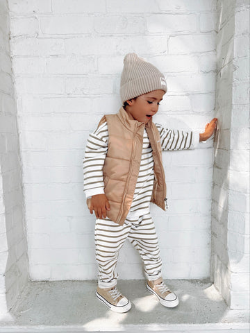4 year old boy wearing green and white striped organic cotton jumper and pants matching set with a Winter brown puffer vest and pom pom beanie with Bobby G branding. 