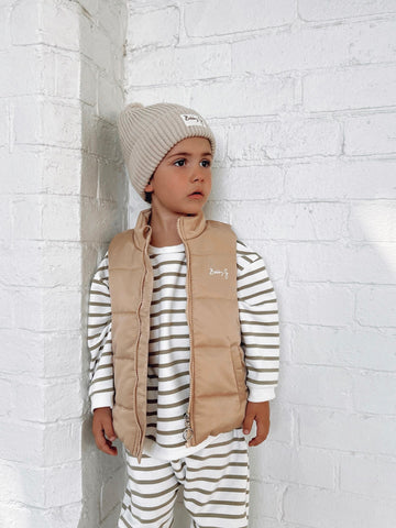 Child wearing green and white jumper and pants paired with a kids puffer Winter vest with Bobby G logo printed in white and a cotton knit pom pom beanie with Bobby G woven label attached. 