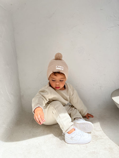 2 year old boy toddler wearing a soft green tracksuit. Jumper featuring a wide fit and white Bobby G embroidery with a cotton knit beanie in neutral hues and a Bobby G woven label attached. 