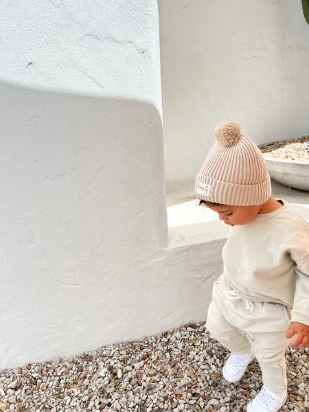 Little boy is wearing a green tracksuit, the oversized jumper has white Bobby G embroidery detail on the front paired with a neutral cotton knit beanie with Bobby G woven label attached. 