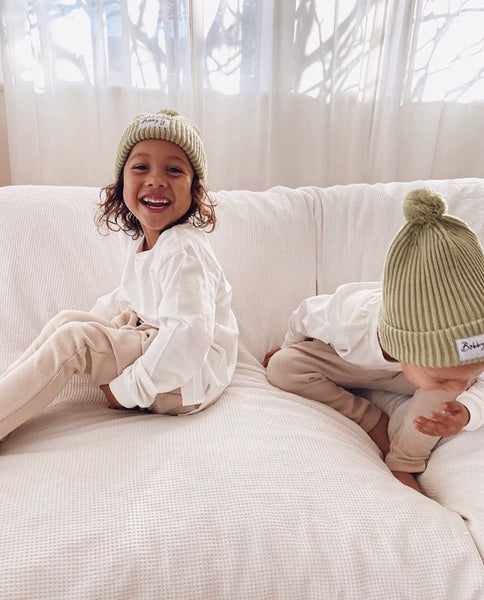 4 and 6 year old boys wearing cotton knit harem pants, white long sleeved tee and a green knit beanie in all neutral colours with Bobby G branding. 